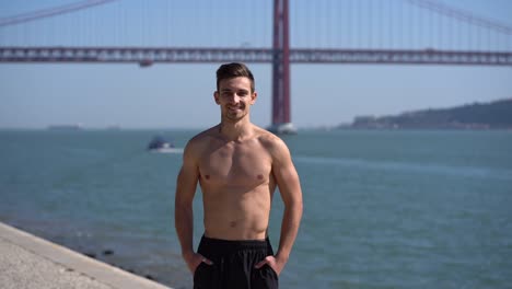 Shirtless-sportsman-standing-near-river-and-smiling-at-camera