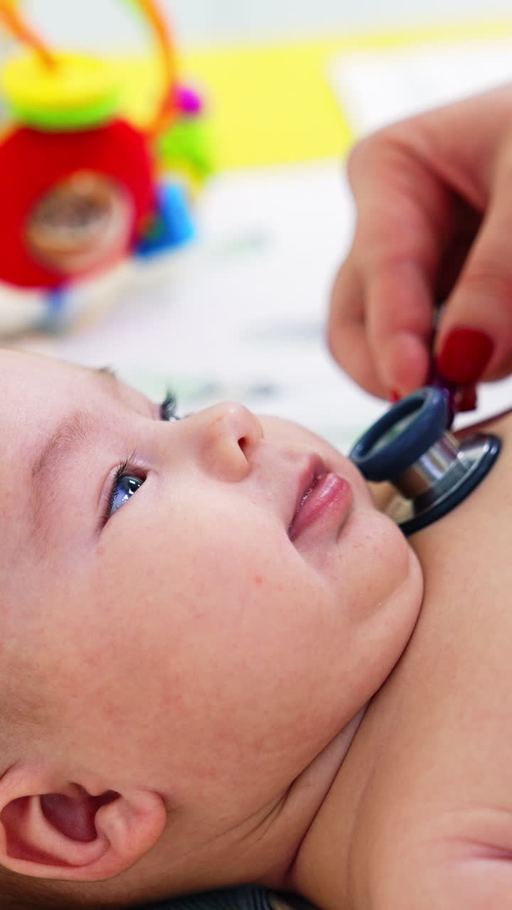 Pediatrician hand puts stethoscope on child's chest. Baby looks interested and smiles to the doctor. Blurred backdrop. Vertical video