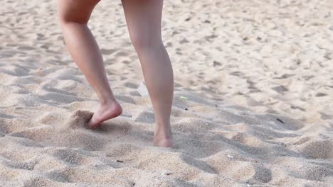 close-up of legs walking barefoot on sunlit sandy beach, capturing movement and texture.