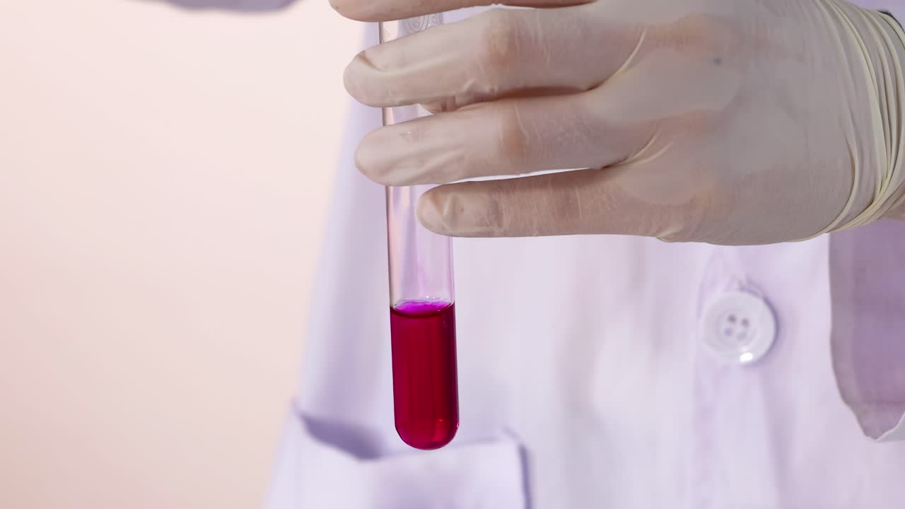 Close-up of gloved hands handling a pink liquid in a test tube with precision.