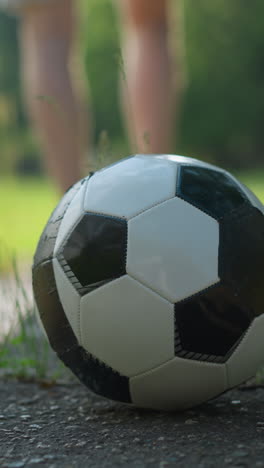 eine verschwommene ansicht von jemandem, der braune shorts und ein rotes oberteil trägt, der von einem auf einer betonoberfläche platzierten fußball wegläuft und zu einem grasbewachsenen feld geht