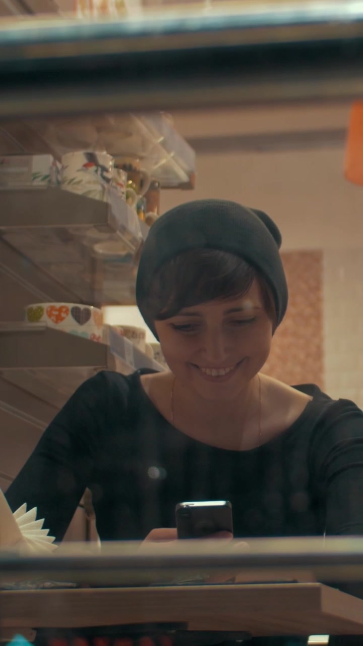 Giovane donna in un bar che digita un messaggio sul cellulare con espressione felice