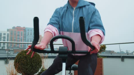 chica atlética realizando ejercicios de entrenamiento de equitación aeróbica en bicicleta bicicleta estacionaria en el techo de la casa