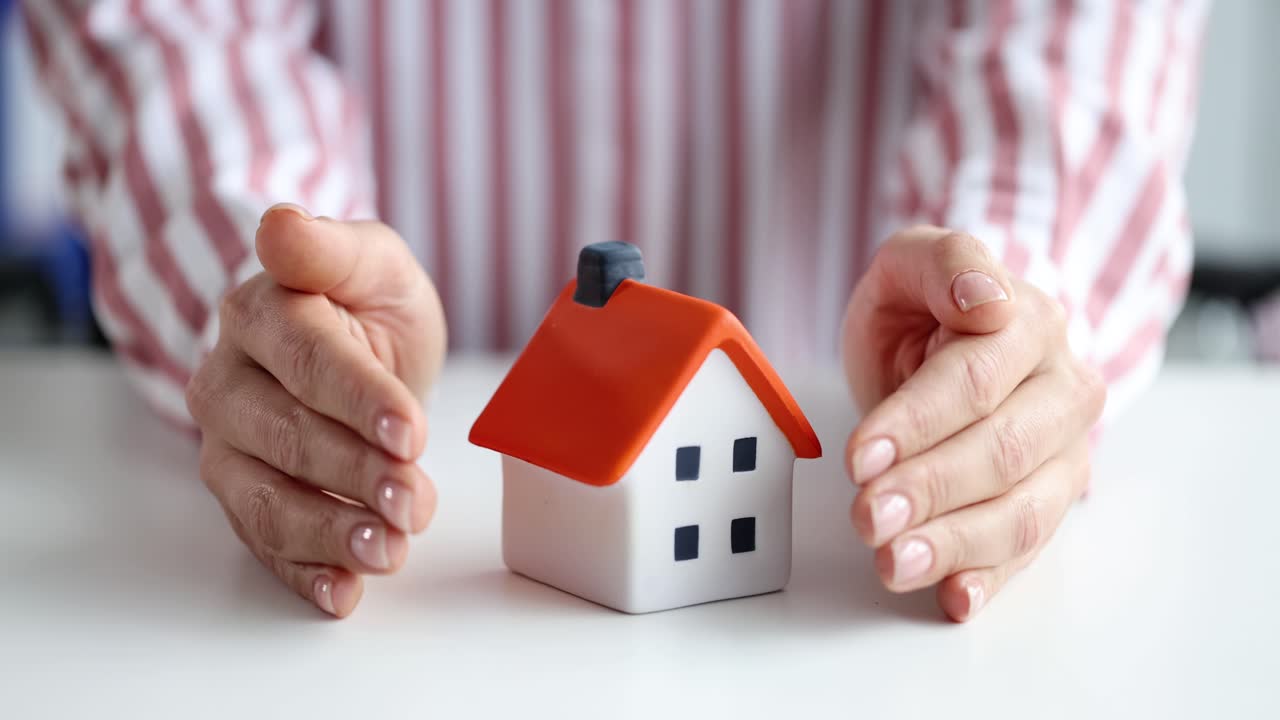 Hands protecting a miniature house, symbolizing home protection or insurance