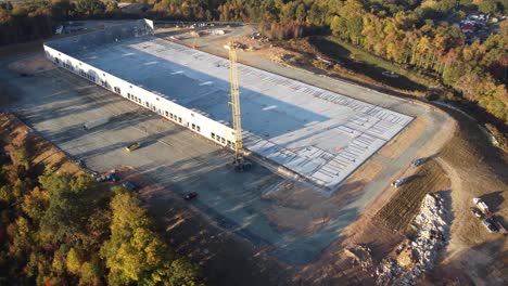 un plano medio desde detrás de una grúa pesada levantando un panel de hormigón en su lugar en un sitio de construcción