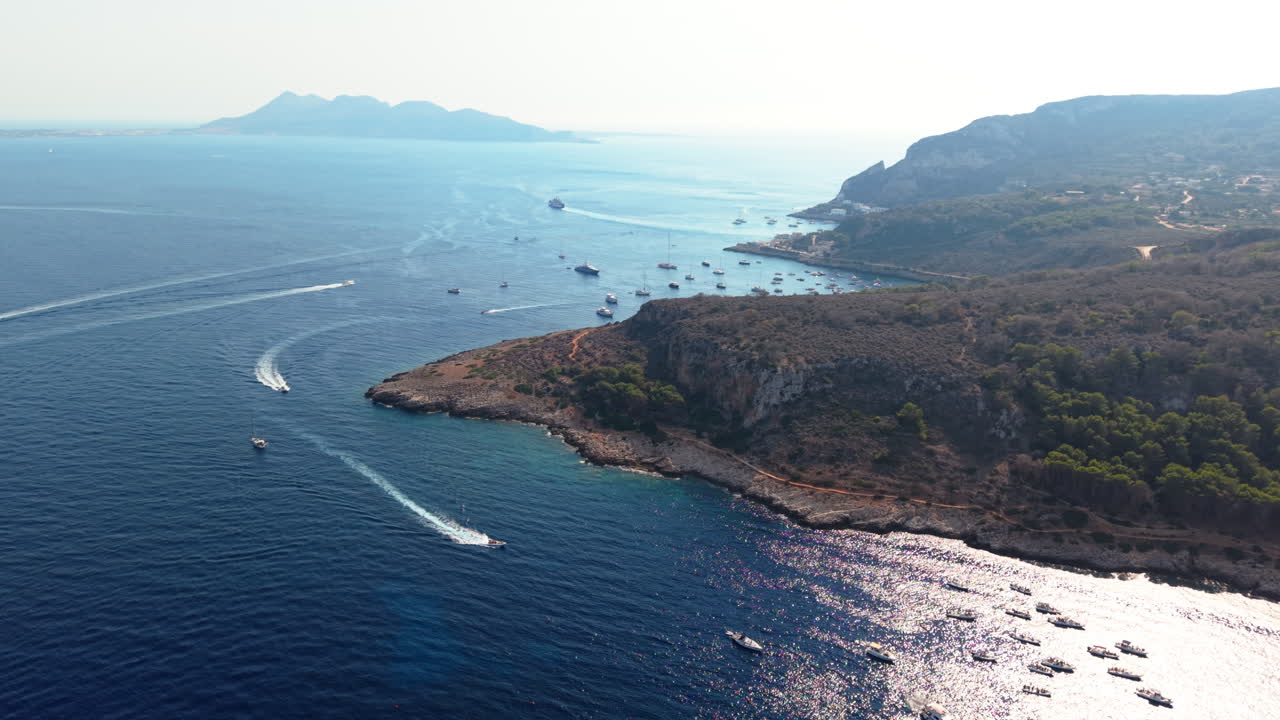 Drone pulls back with slight orbit showing Sicilian coastline, wild beaches, boats and mountains
