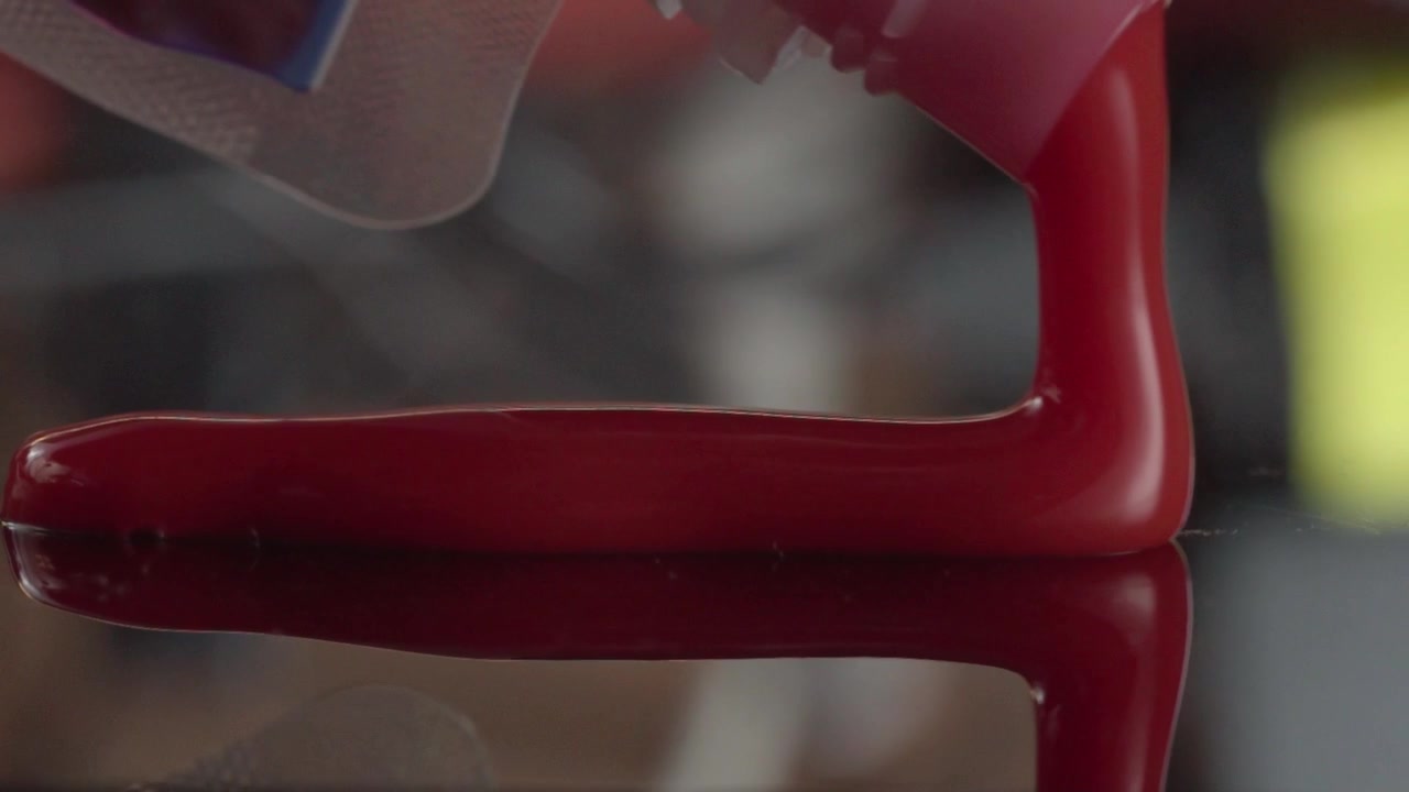 Un primo piano macro mostra vernice acrilica rossa lucida che forma una forma curva liscia su una superficie riflettente, con riflessi morbidi e dettagli dello sfondo sfocati