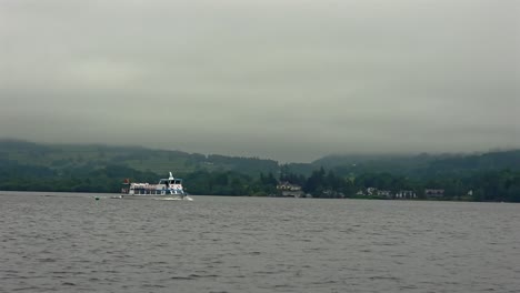 Wide shot of a boat sailing on Lake Windermere with fog over distant hills.