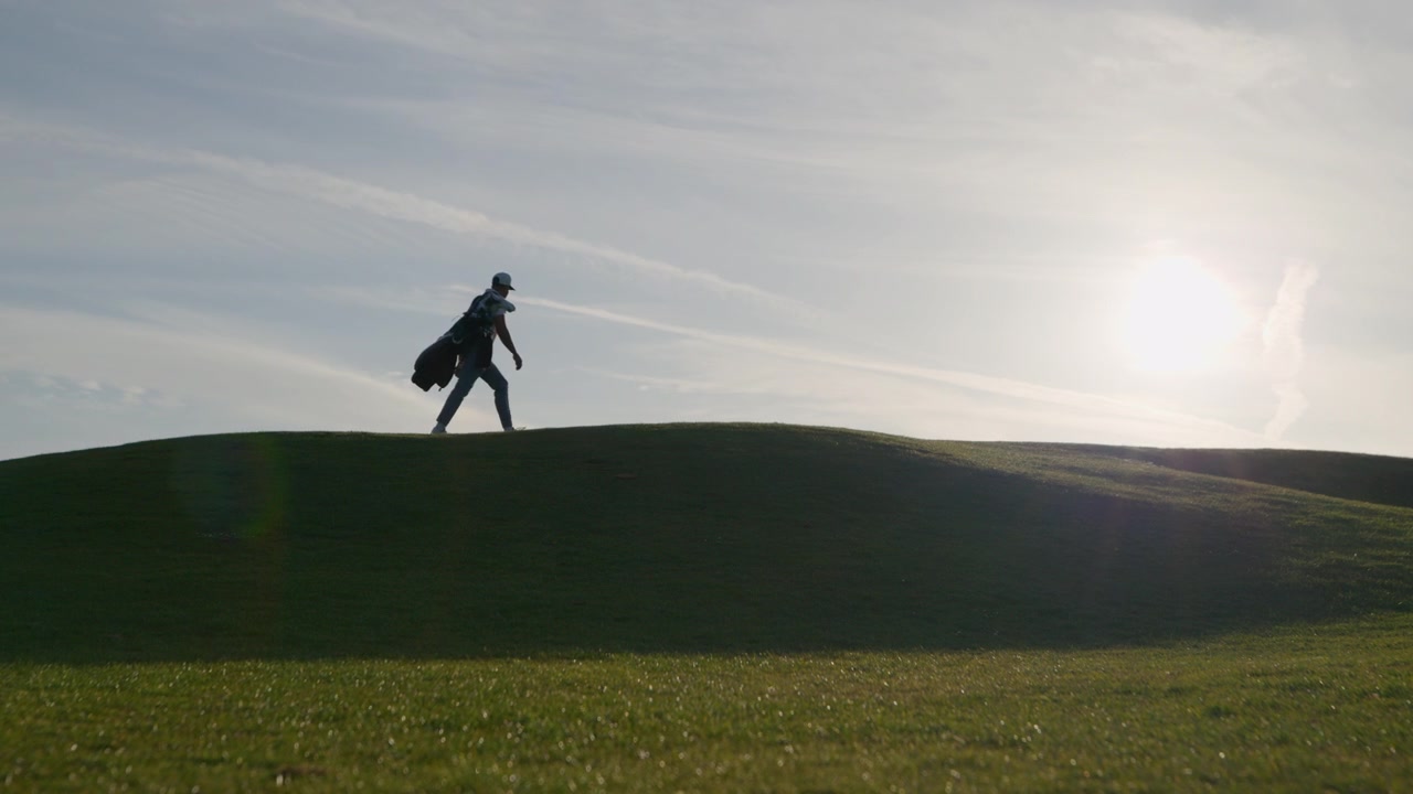 Golfer walking golf course during sunrise backlit