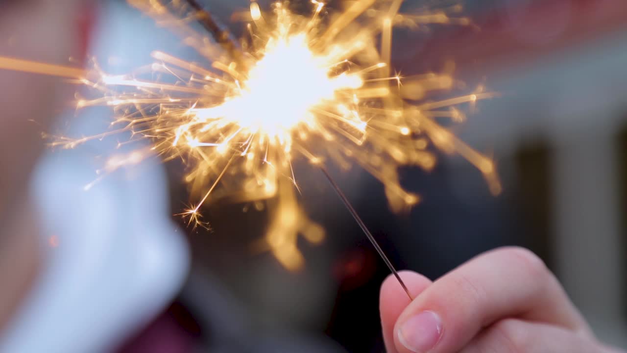 primer plano de una mano sosteniendo una chispa encendida, con chispas brillantes volando, fondo borroso