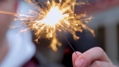 Close-up-of-a-hand-holding-a-lit-sparkler,-with-bright-sparks-flying,-blurred-background