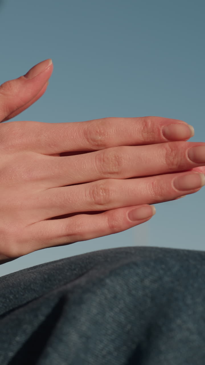 한 사람의 손이 부드럽게 어지는 클로즈업, 깊은 상이나 생각을 나타니다. 그 사람의 얼굴은 보이지 않으며, 단지 청바지와 갈색 코트만 보입니다.