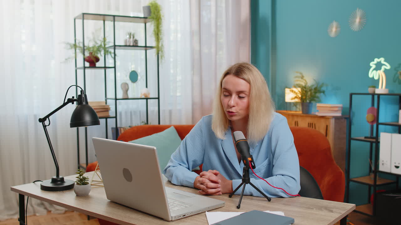 Happy blogger woman recording podcast at table giving workshop webinar speaking at microphone laptop