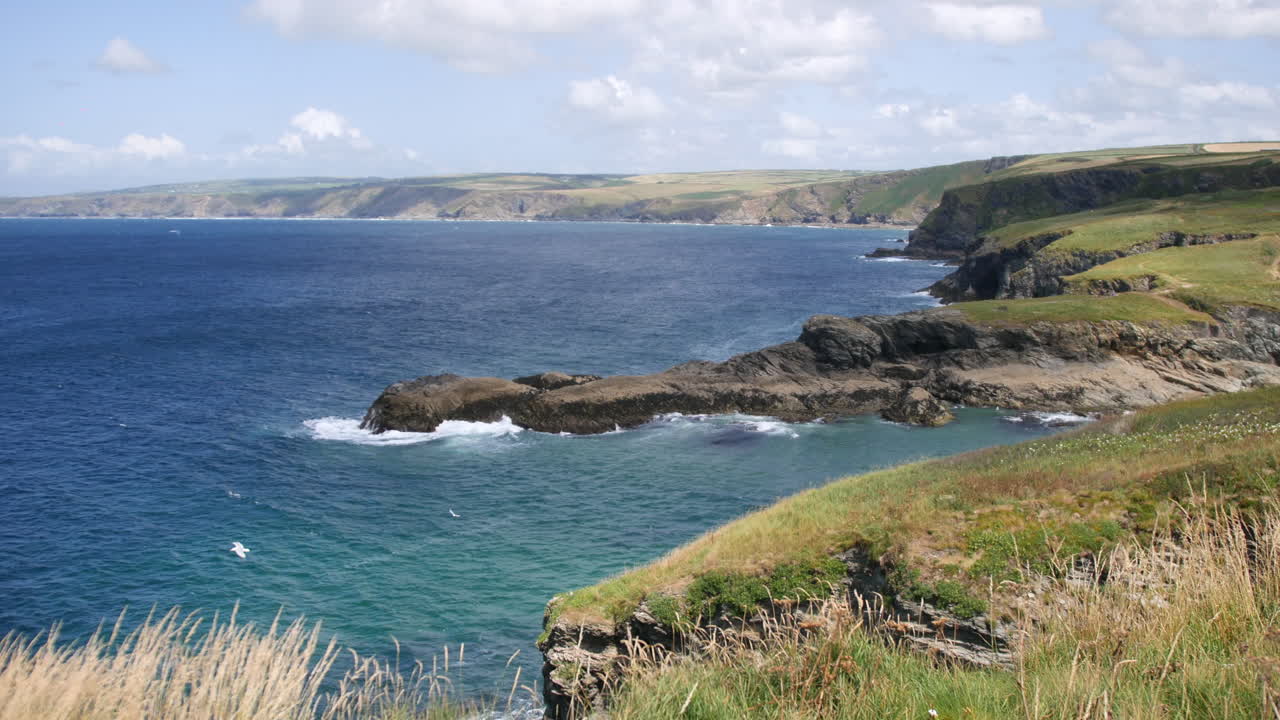English coastline with jagged rocks and turquoise water is curving through the Cornwall landscape, showing the natural beauty near Port Isaac and the fictional Portwenn