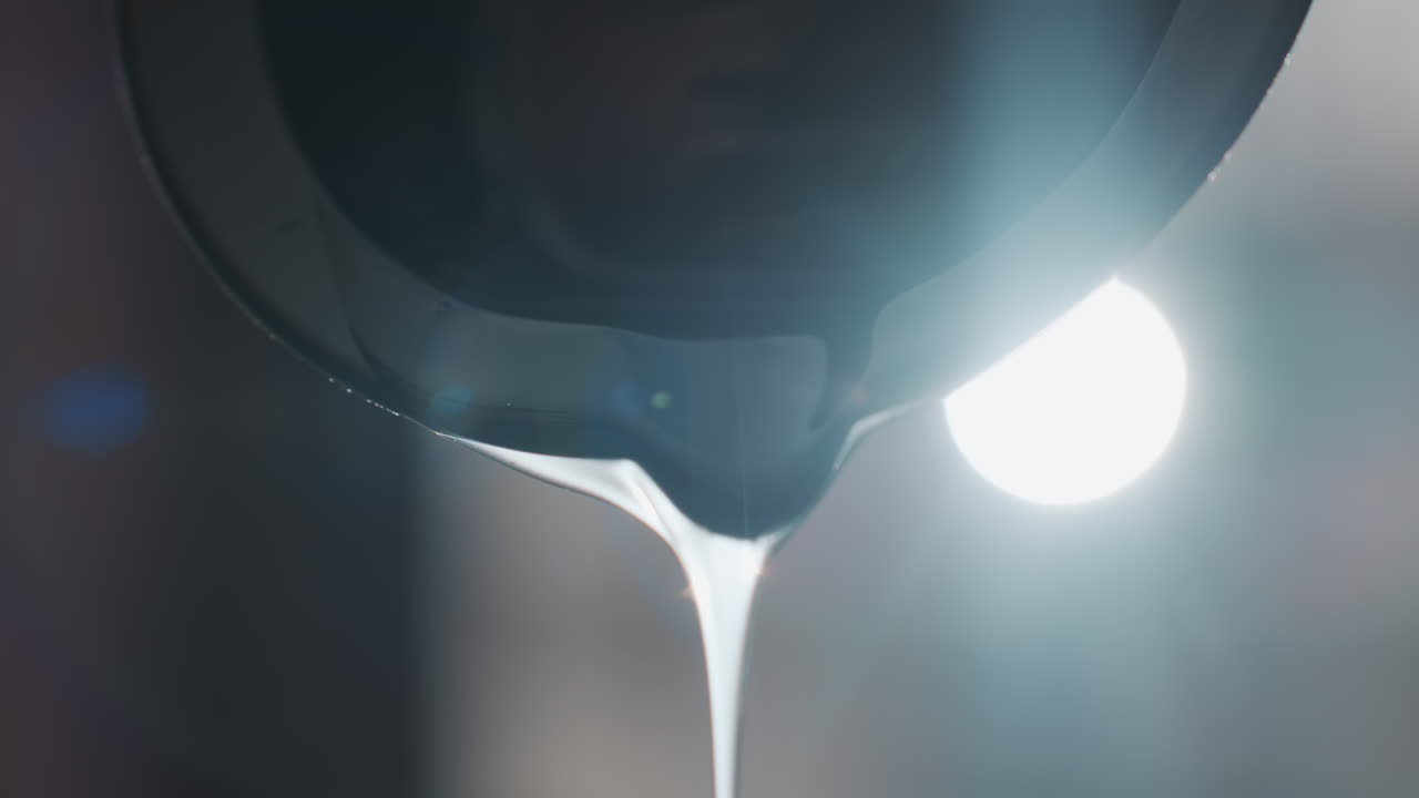 병에 액체가 쏟아지는 역광 클로즈업, 윤기 있는 흐름과 밝은 테두리 조명, 스튜디오 하이라이트와 반사되는 표면, 투명한 텍스처와 발광하는 분위기로 천천히 꾸준히 떨어지는 액체