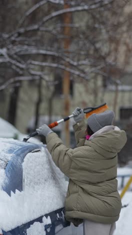 woman removing snow from car in winter