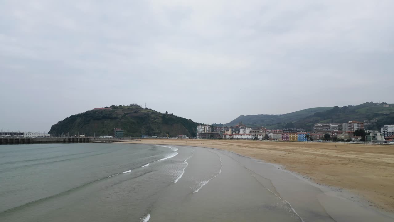 Wavy sea washing sandy coast under overcast sky in Cantabria, Spain