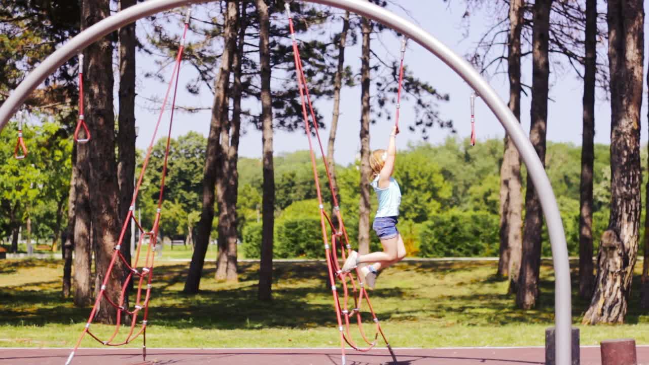 niña en el patio de recreo, jugando en barras de mono y cuerda, saltando hacia abajo
