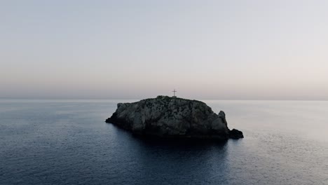 aerial footage flying towards and over a cross on the small island of scoglio dell'eremita in southern italy