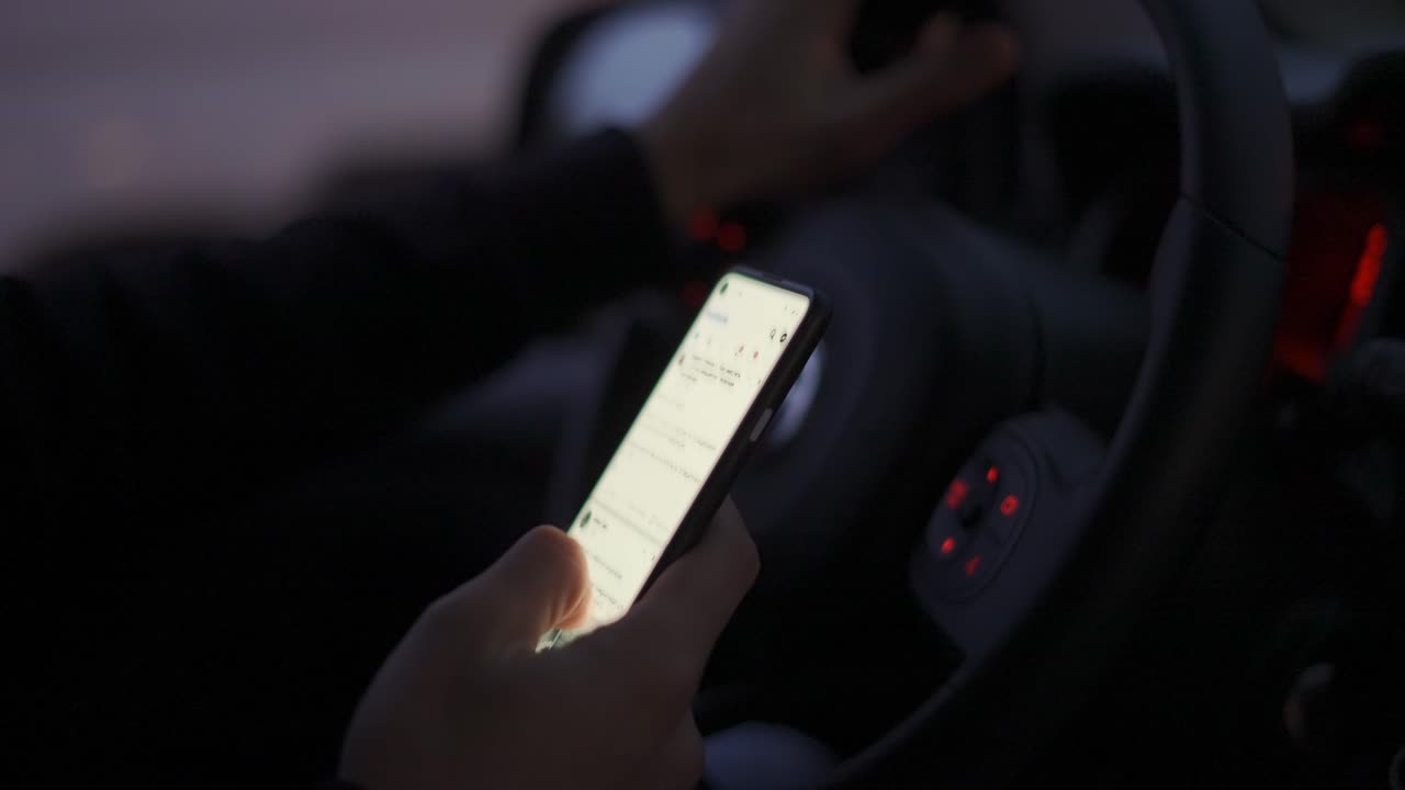 hombre irreconocible desplazándose ilegalmente en su teléfono móvil durante la conducción por la noche