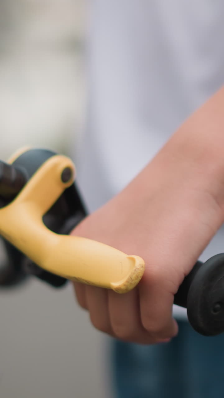 un primer plano de la mano de un niño agarrando una palanca de freno amarilla en el manillar de una bicicleta