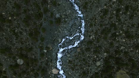 aerial top down view of water stream flowing on dry mountain river bed in alpe ventina of valmalenco in northern italy