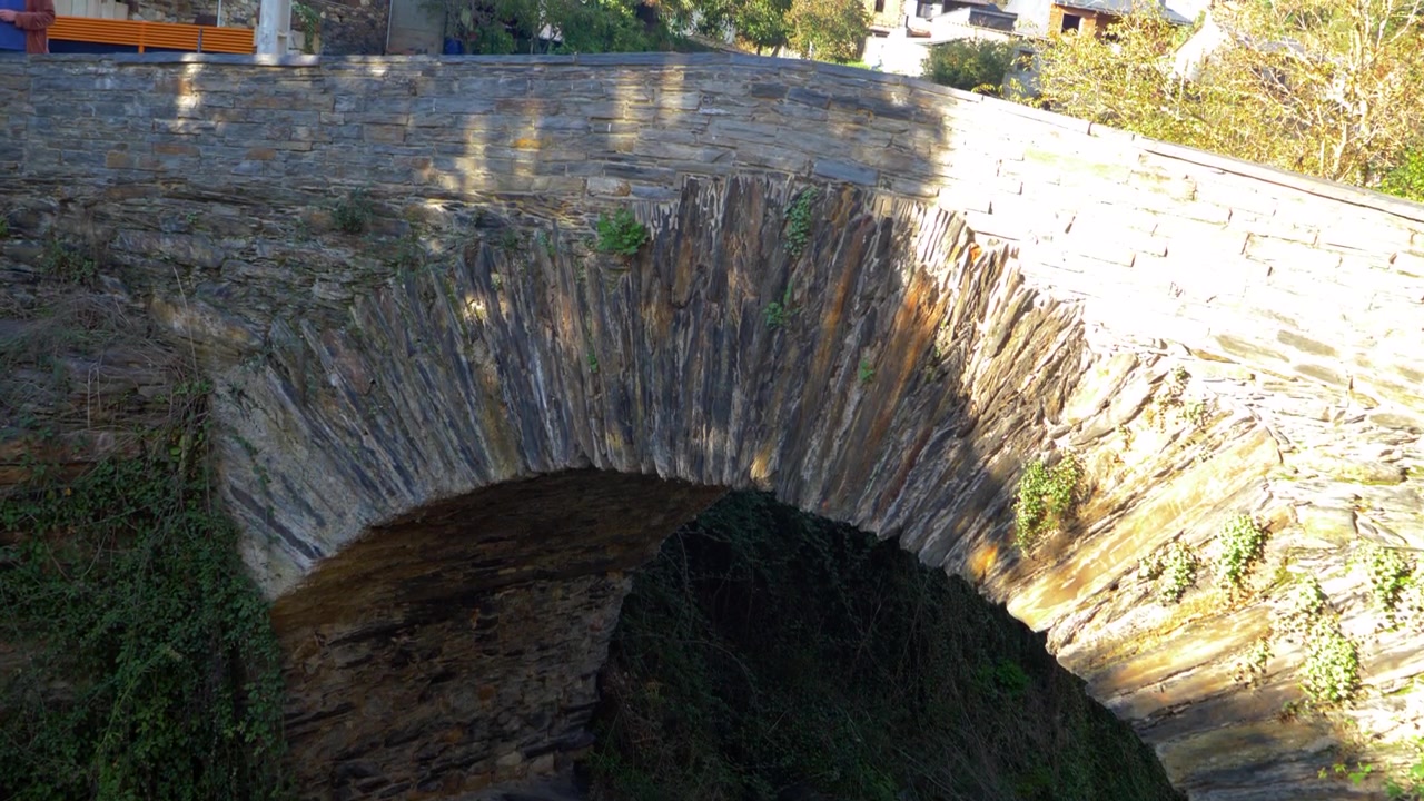 Muratura e arco di ponte romano brillano alla luce del sole sopra il burrone a Éntoma, Galizia