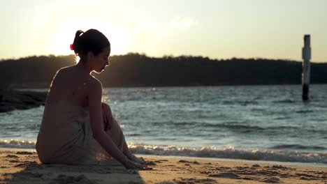 Junge-Frau-Betrachtet-Während-Eines-Sonnenuntergangs,-Während-Sie-Am-Strand-Sitzt