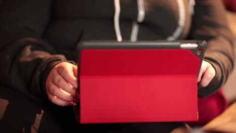 girl's hand's typing on a red tablet in her living room