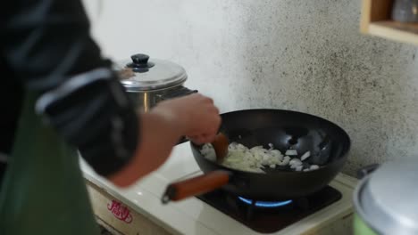 freshly cut onions fried in black fry pan and stirred by hand with wooden spoon, filmed as closeup slow motion style shot