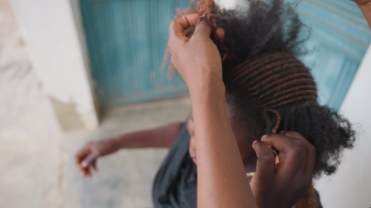 Primo piano di apprendista afroamericana che misura la sezione dei capelli, pettine che allinea file ordinate sul cuoio capelluto in un ambiente stradale esterno, tecnica concentrata, tensione attenta, dita che guidano il motivo intrecciato, energia da tutorial.