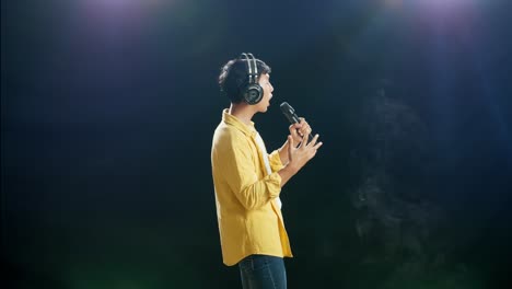 vista lateral de un joven asiático con auriculares sosteniendo un micrófono y cantando sobre el fondo blanco de humo negro