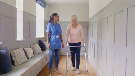 senior woman at home using walking frame being helped by female care worker in uniform