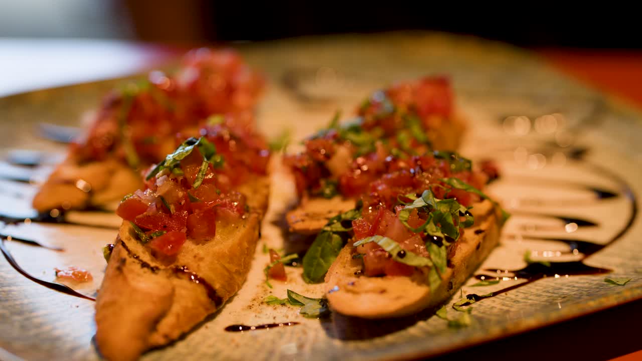 Close-up of hand picking bruschetta appetizer with tomato, basil, and balsamic drizzle in warm lighting