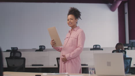 portrait of a smiling pregnant woman caressing her belly and smiling at camera in the office