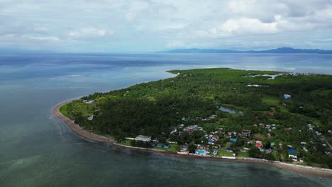 aerial pullback of idyllic tropical philippines island coastline with small village and lush greenery