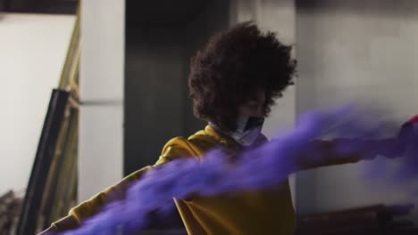 mixed race woman holding blue and purple flares dancing in an empty building