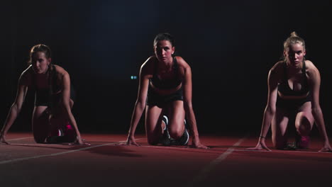 three sports girl athletes at night on the treadmill start for the race at the sprint distance from the sitting position