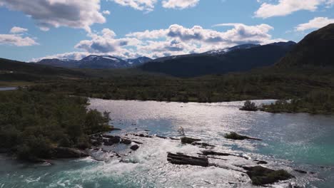 Aerial-view-of-a-river-flowing-through-a-valley-and-creating-waterfalls,-surrounded-by-mountains-and-forests-in-norway