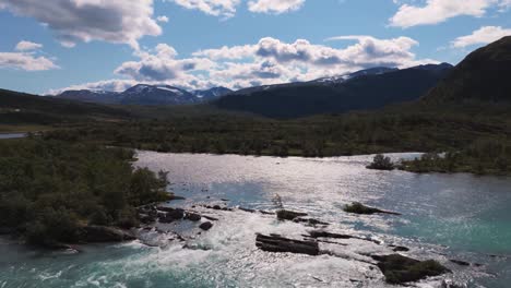 vista aérea de un río que fluye a través de un valle y crea cascadas, rodeado de montañas y bosques en noruega