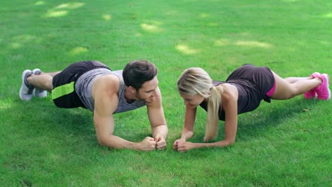 Glücklicher-Mann-Und-Frau-Stehen-Beim-Fitnesstraining-Im-Freien-Auf-Einer-Planke-Auf-Grünem-Gras