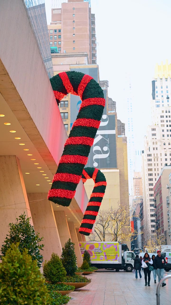 New York, USA, 4 gennaio 2026: Bastoncini di zucchero giganti si stagliano sopra un marciapiede di New York durante il periodo natalizio. Decorazioni a forma di gancio rosse e verdi sporgono dalla facciata di un edificio sopra degli arbusti