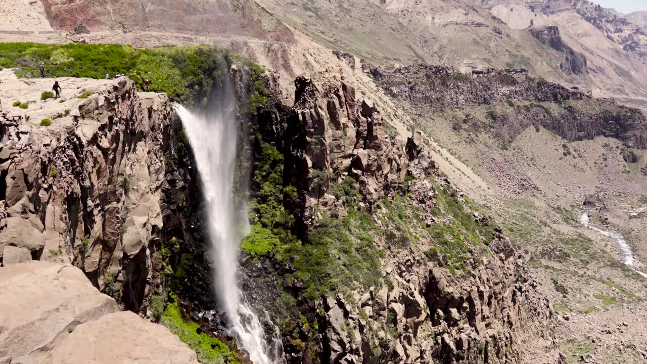 Veduta generale della cascata invertita, fortemente spinta dal vento, con la scogliera circostante caratterizzata dall'aridità delle montagne del Cile centrale.