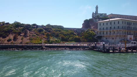 Toma-Panorámica-De-Primer-Plano-Del-Cardán-Del-Muelle-De-Aterrizaje-Y-El-Centro-De-Bienvenida-En-La-Isla-De-Alcatraz-Desde-Un-Barco-En-Movimiento-En-La-Bahía-De-San-Francisco