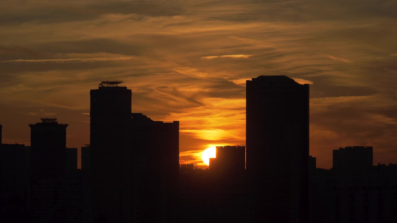 Atardecer naranja dorado con el sol poniéndose detrás del horizonte urbano silueteado y rascacielos, con nubes dramáticas, ideal para viajes de negocios urbanos al atardecer y fondos cinematográficos.