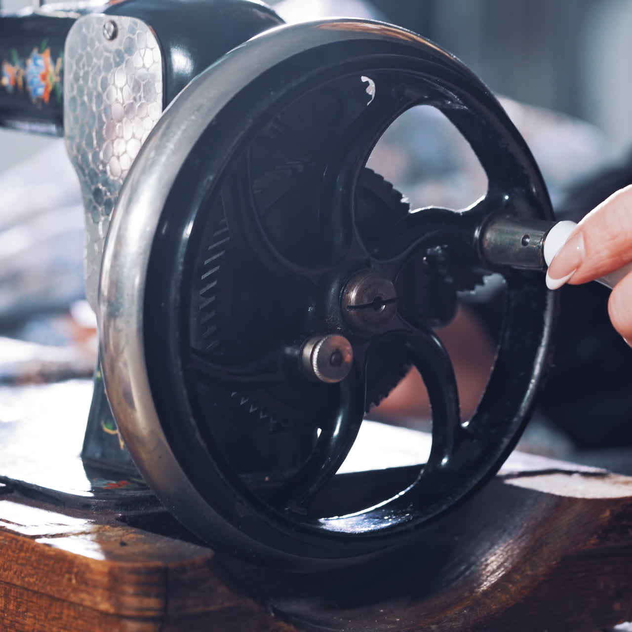 Close-up of woman's hand spinning the metal wheel of an old sewing machine. Seamstress is working on a black sewing machine in atelier. Craft and handmade concept.