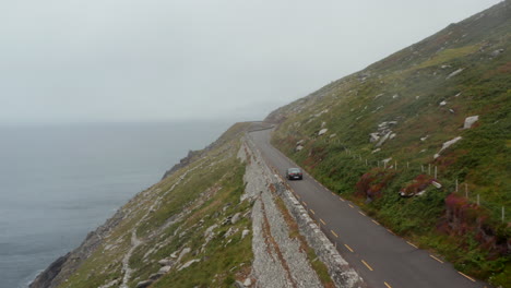 Single-car-driving-on-narrow-panoramic-route-high-above-sea-coast.-Road-with-many-sharp-turns.-Hazy-day-in-landscape.-Ireland