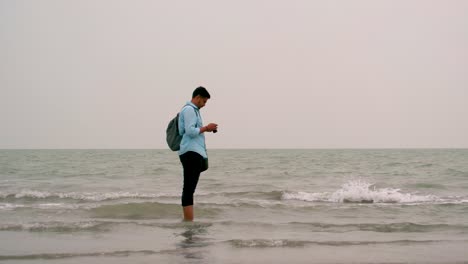 travel photographer with camera standing at the scenic beach with rough waves