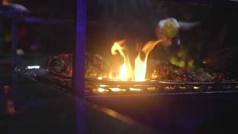 Behandschuhte-Hände,-Die-Nachts-Gebratenes-Hähnchen-über-Einem-Feuergrill-Wenden,-Mittlere-Nahaufnahme