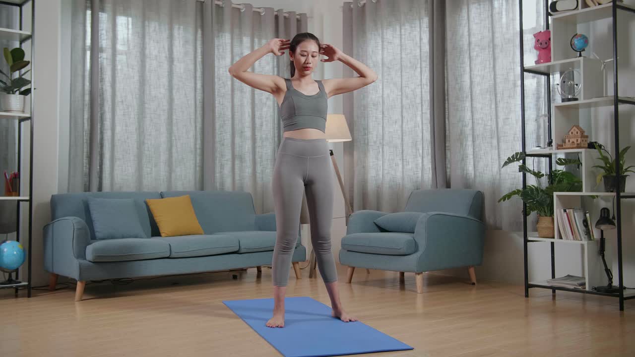 젊은 아시아 트레이너 여성 스포츠 옷을 입고 집에서 운동을 가르치는 동안 말하고 심장 운동을 하는 전체 시각